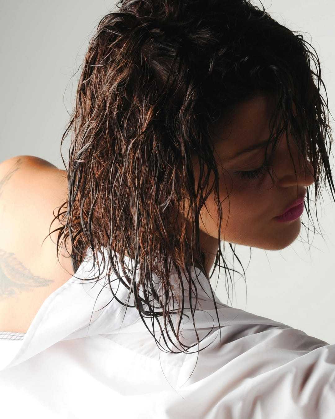 Woman with wet hair, wearing a white shirt, looking down with a pensive expression.