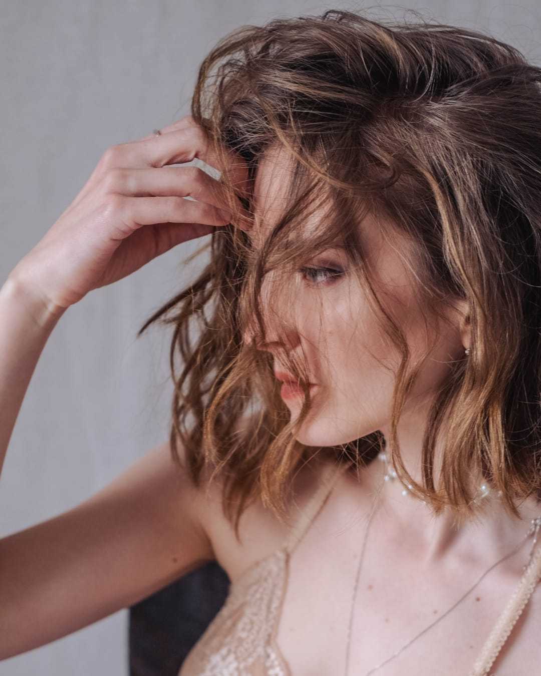 Woman with tousled hair gazing to the side, wearing a delicate lace top and a choker necklace.