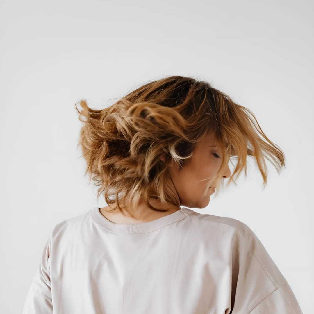 Woman with short, wavy hair in motion, wearing a white shirt against a plain background.