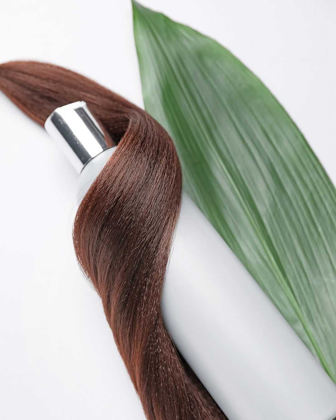 Shampoo bottle with a strand of hair wrapped around it, placed beside a green leaf.