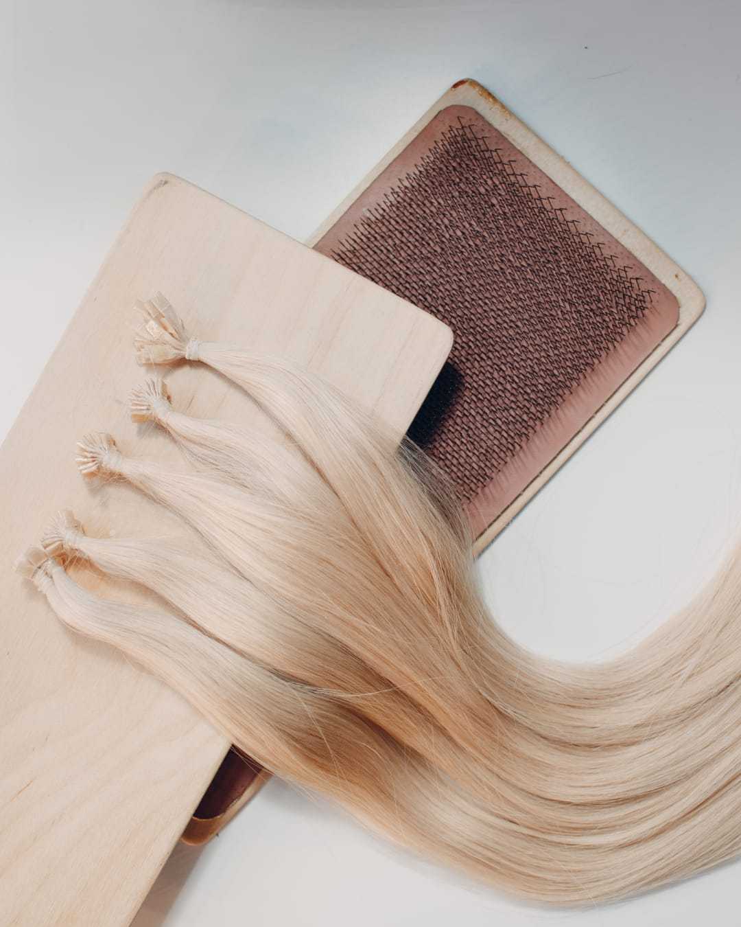 Blonde hair extensions on a wooden board with a hairbrush nearby.